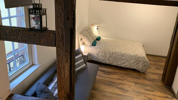 Una habitación pequeña y acogedora con una cama, un banco y un ventanal.