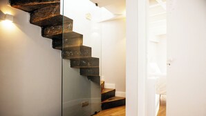 Una escalera con barandillas de vidrio y peldaños de madera, que conduce a una habitación con paredes blancas y suelo de madera.