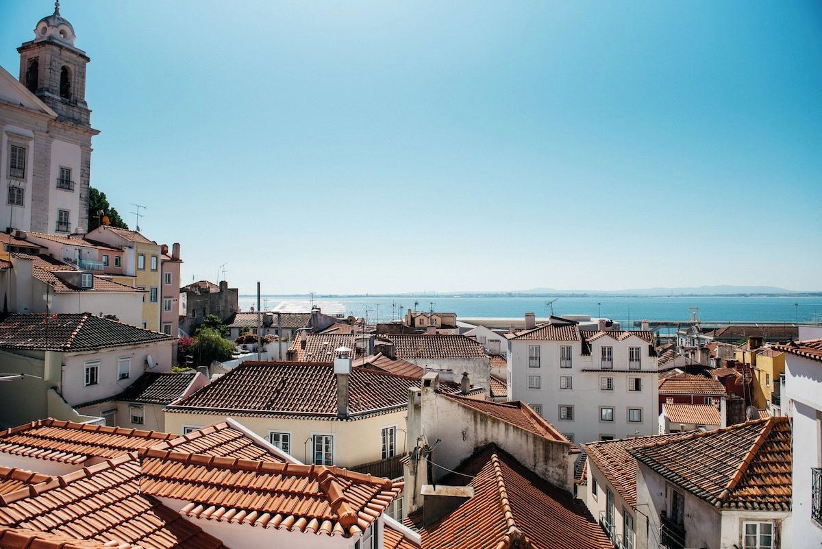 Un paysage urbain côtier avec des bâtiments aux toits de tuiles rouges et un clocher d’église imposant.