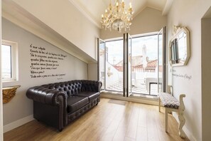 A modern living room with a leather sofa, a bench, a chandelier, and a large window with a view of buildings. - Portuguese Soul Alfama|XL Rooftop & River View 20p (Lisboa)