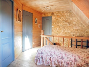 Ein Schlafzimmer mit Holzbalkendecke, Steinwand und einem Bett mit floralem Bettbezug.