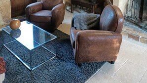 Een landelijke woonkamer met leren fauteuils, een glazen salontafel, een open haard en een stenen muur.