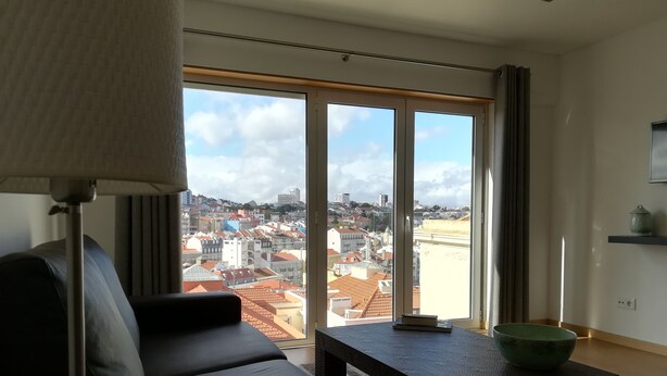 Una sala de estar moderna con sofá, mesa de centro y vistas a un paisaje urbano a través de amplios ventanales.