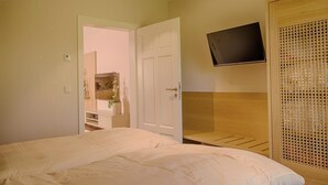 A hotel room with a bed, a TV mounted on the wall, and a wooden wardrobe.