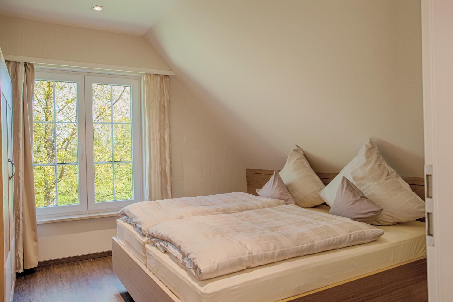 A bedroom with a large window, a bed with a wooden headboard, and a bedside table.