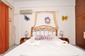 A neatly made bed with white linens, a decorative headboard, and a floral arrangement. There are two bedside tables with lamps and a wooden wardrobe. - Manos Syros (Syros)