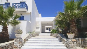 Un bâtiment blanc avec des balcons bleus, des marches en pierre et des plantes en pot.
