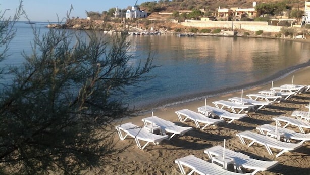Une plage avec des chaises longues blanches et un petit bâtiment blanc en arrière-plan.