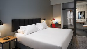 A modern hotel room with a large bed, bedside tables, a desk, and a bathroom visible through an open door. - The Pop Hotels (Santiago)