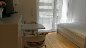 Una stanza con un letto bianco, un tavolino con una poltrona floreale e una finestra con tende leggere.