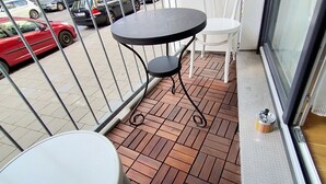 Un balcone con pavimento piastrellato, un tavolo rotondo, una sedia bianca e una ringhiera in metallo.