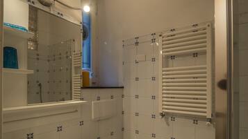 Un baño con lavamanos, inodoro y espejo. Hay una ventana con persianas y una zona de ducha.