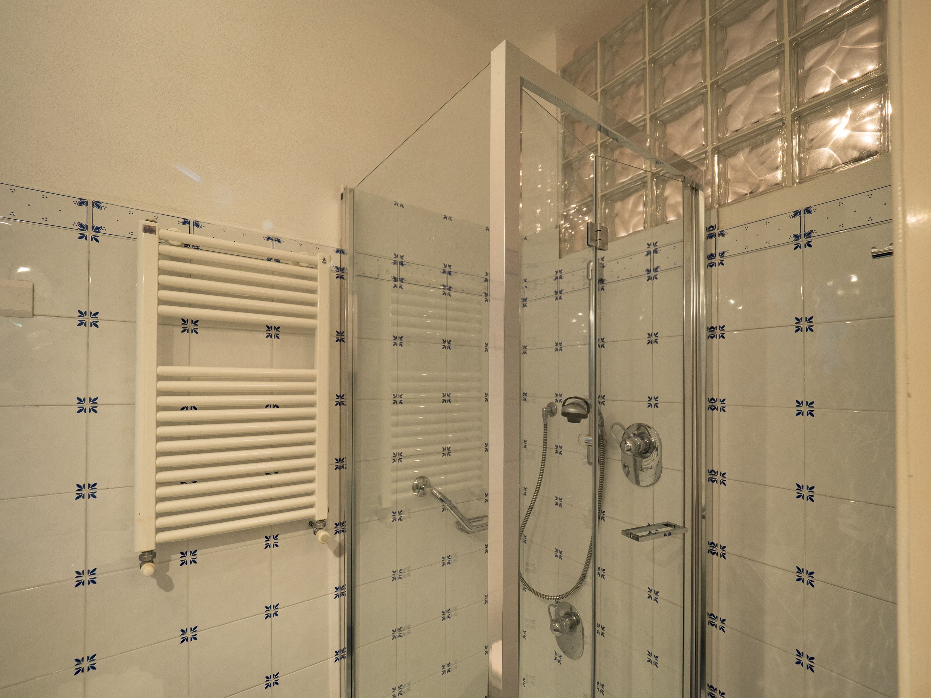 A glass-enclosed shower with a handheld showerhead and a handheld faucet.