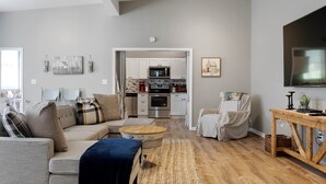 A modern living room with a sofa, a coffee table, and a chair. There is a kitchen in the background with a microwave and oven. - Lyric Guesthouse at GratiDude Ranch - Riverside in Leiper's Fork (Franklin)