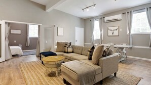 A modern living room with a beige sofa, a round coffee table, and a dining area with a white table and chairs. - Lyric Guesthouse at GratiDude Ranch - Riverside in Leiper's Fork (Franklin)