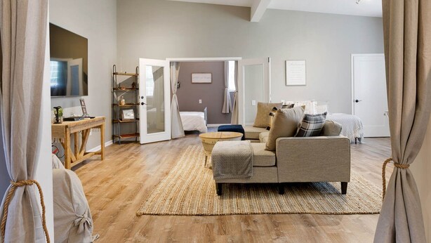 A spacious living room with a sofa, a coffee table, and a TV. There is a wooden floor and a door leading to another room. - Lyric Guesthouse at GratiDude Ranch - Riverside in Leiper's Fork (Franklin)