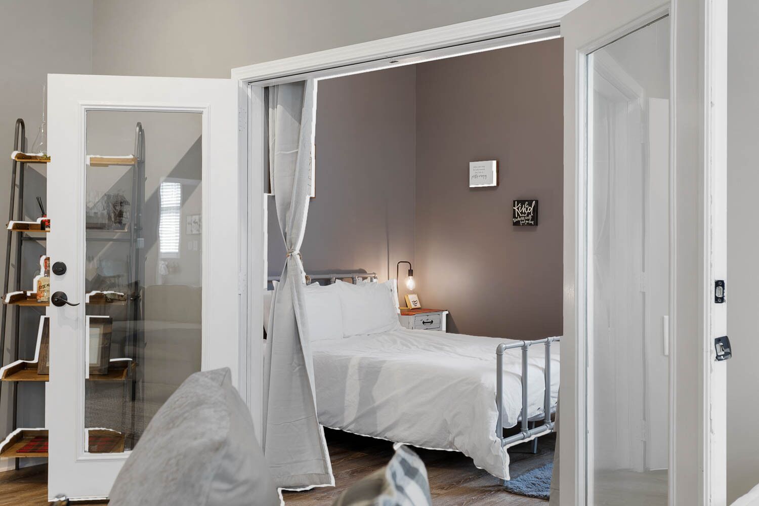 A bedroom with a bed, a bedside table, a lamp, a wardrobe, and a glass door.