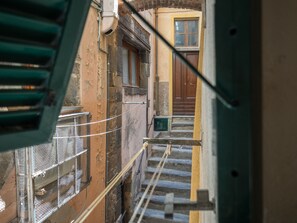 A narrow stairway leading to a wooden door, with a metal railing on one side and a building facade with peeling paint and a window. - Rundanina Village Life Studio (Vernazza)