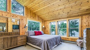 Une chambre aux murs lambrés, avec un lit, une commode, un téléviseur et de grandes fenêtres.