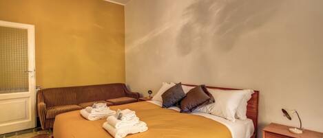 A hotel room with a bed, a bench, a bedside table, and a chandelier.