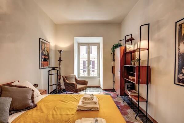 A bedroom with a bed, a chair, a window, and a bookshelf.