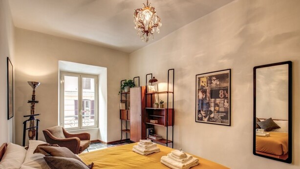 A hotel room with a bed, a chair, a bookshelf, and a chandelier. - Trastevere Vintage (Rome)