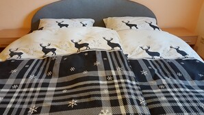 Una cama con una manta a cuadros y almohadas con motivos de ciervos y copos de nieve.