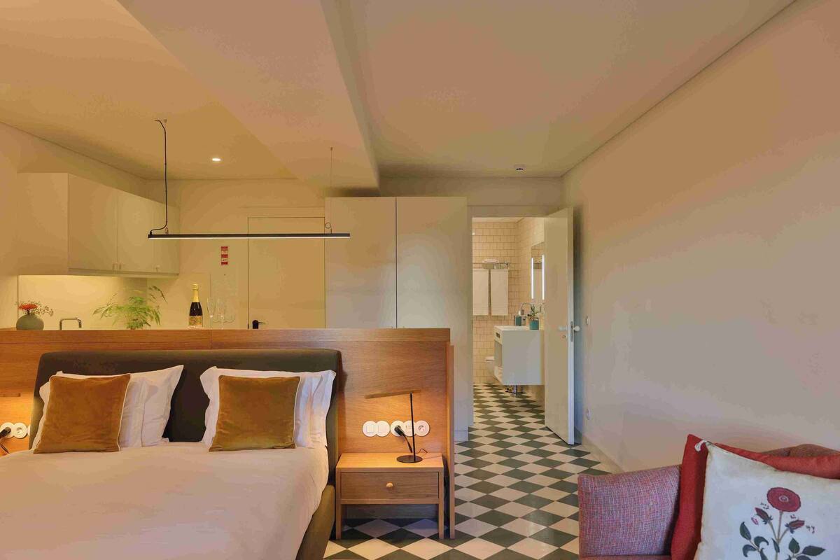 A hotel room with a large bed, a wooden headboard, a bedside table with a lamp, and a checkered floor.