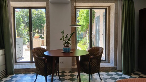 Une pièce avec un sol à carreaux, une table ronde entourée de chaises, une plante en pot et de grandes fenêtres avec des rideaux.