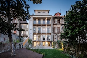 A multi-story building with a courtyard, featuring a staircase, a wooden deck, and a well-maintained garden. - Menina Colina Guesthouse (Porto)