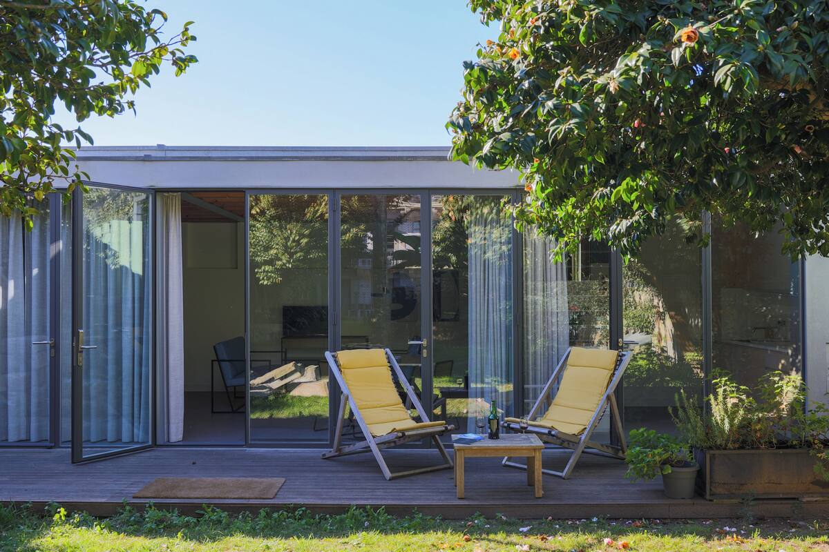 A modern house with a glass door leading to a deck with two yellow lounge chairs and a small table.