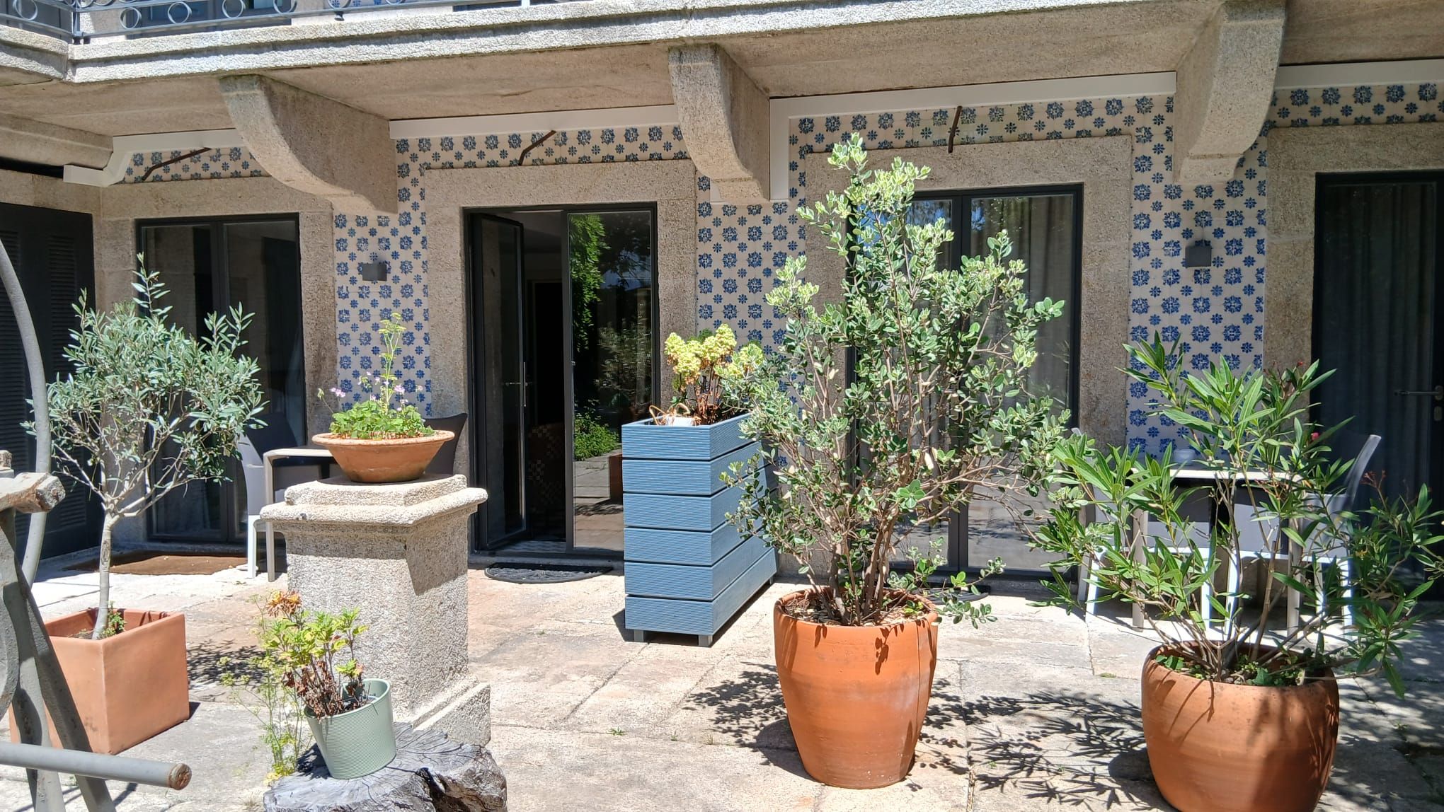Une cour avec des plantes en pot, un banc en pierre et un jardinier bleu.
