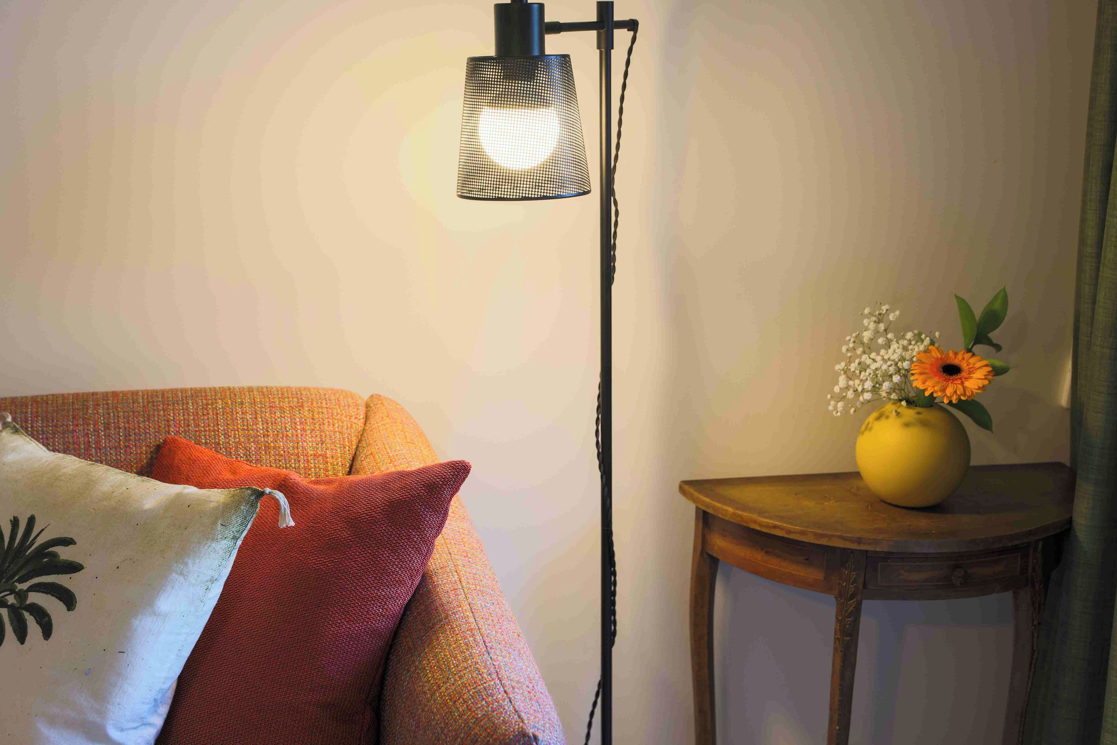 Una habitación con un sofá, una lámpara de pie y una mesita con un jarrón de flores.