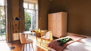 A hotel room with a bed, a desk with chairs, a wardrobe, and a balcony with a table and chairs. - Menina Colina Guesthouse (Porto)