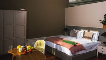 Quarto com cama, mesa de cabeceira e uma cadeira de madeira. Há um guarda-roupa e uma planta na parede.