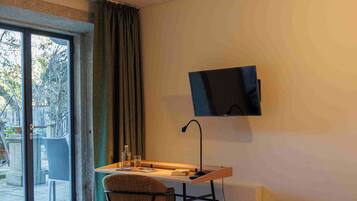 Habitación de hotel con cama, escritorio con silla, televisor montado en la pared y una ventana grande con cortinas.