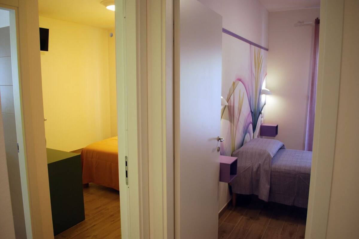 A bedroom with two beds, a bedside table, a lamp, and a wall-mounted shelf.