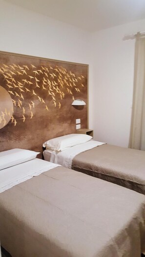 A hotel room with two beds, a wall-mounted lamp, and a decorative wall piece. - B&B Angelo (Ascoli Piceno)