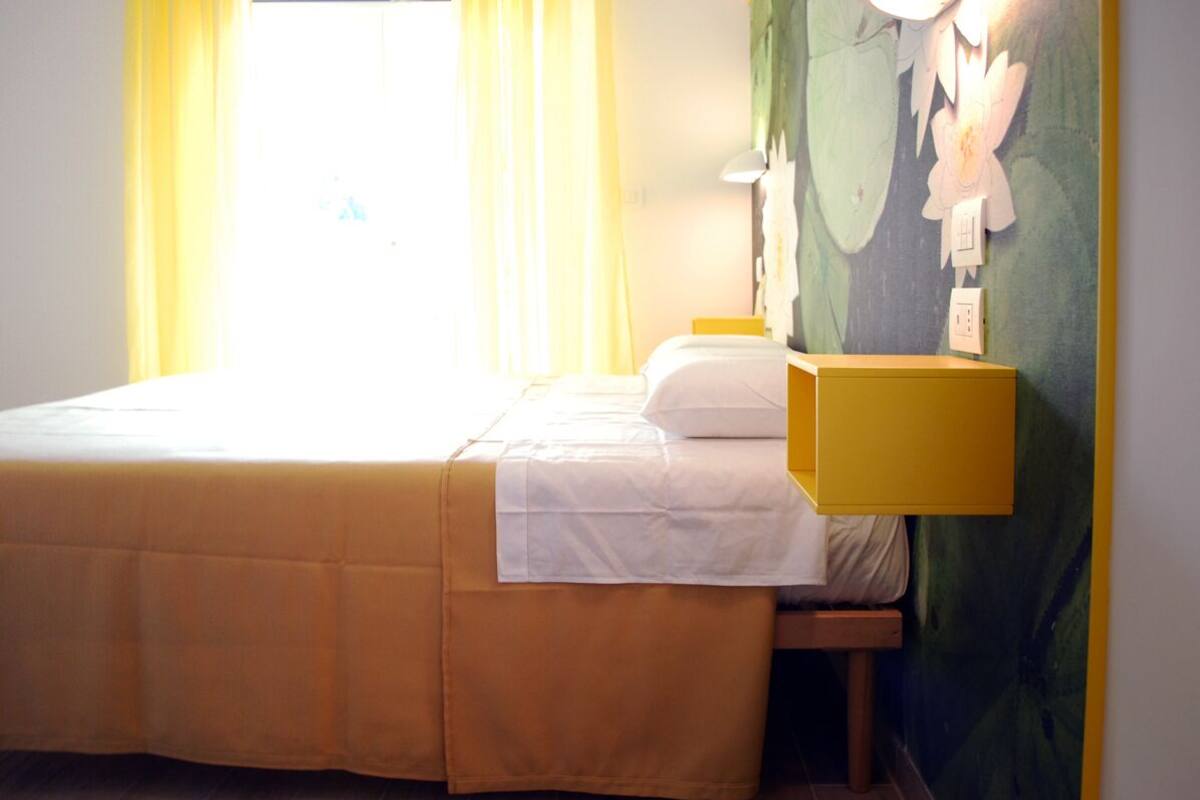 A hotel room with a bed, a nightstand, a lamp, and a wall with a floral mural.