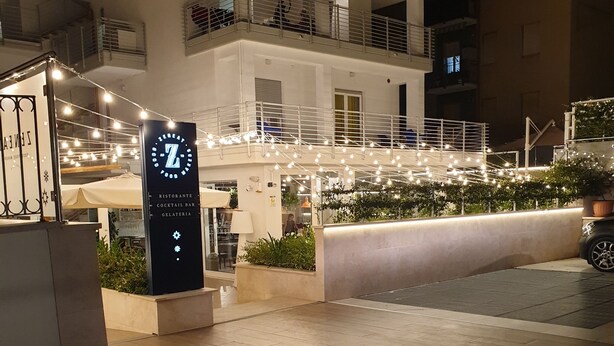 A modern building with a balcony, a signboard, and a paved area with plants. - B&B Angelo (Ascoli Piceno)