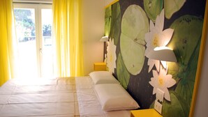 A hotel room with a bed, yellow curtains, a wall with a lotus flower mural, and a nightstand with a lamp. - B&B Angelo (Ascoli Piceno)