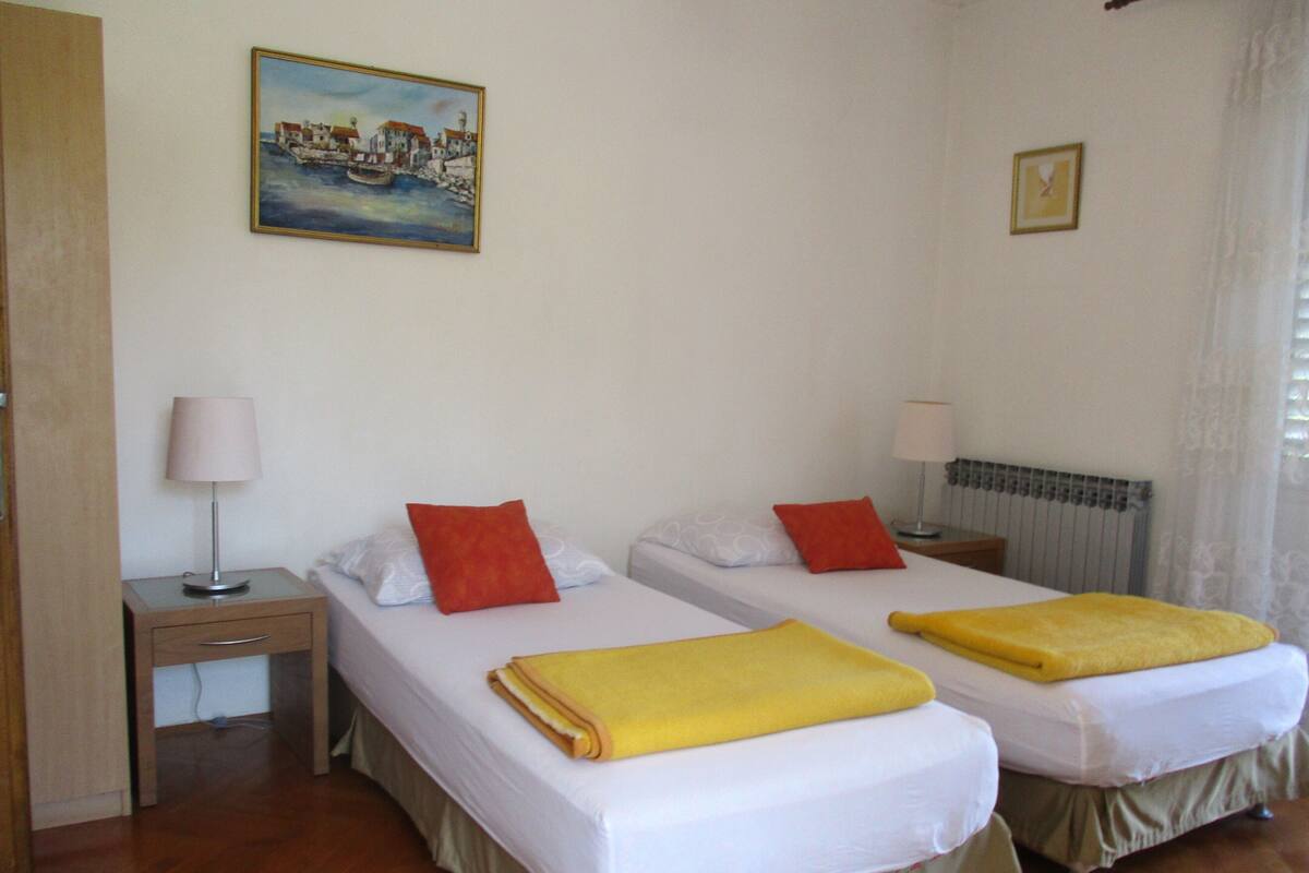 A hotel room with two beds, a painting on the wall, a window with curtains, and a radiator.