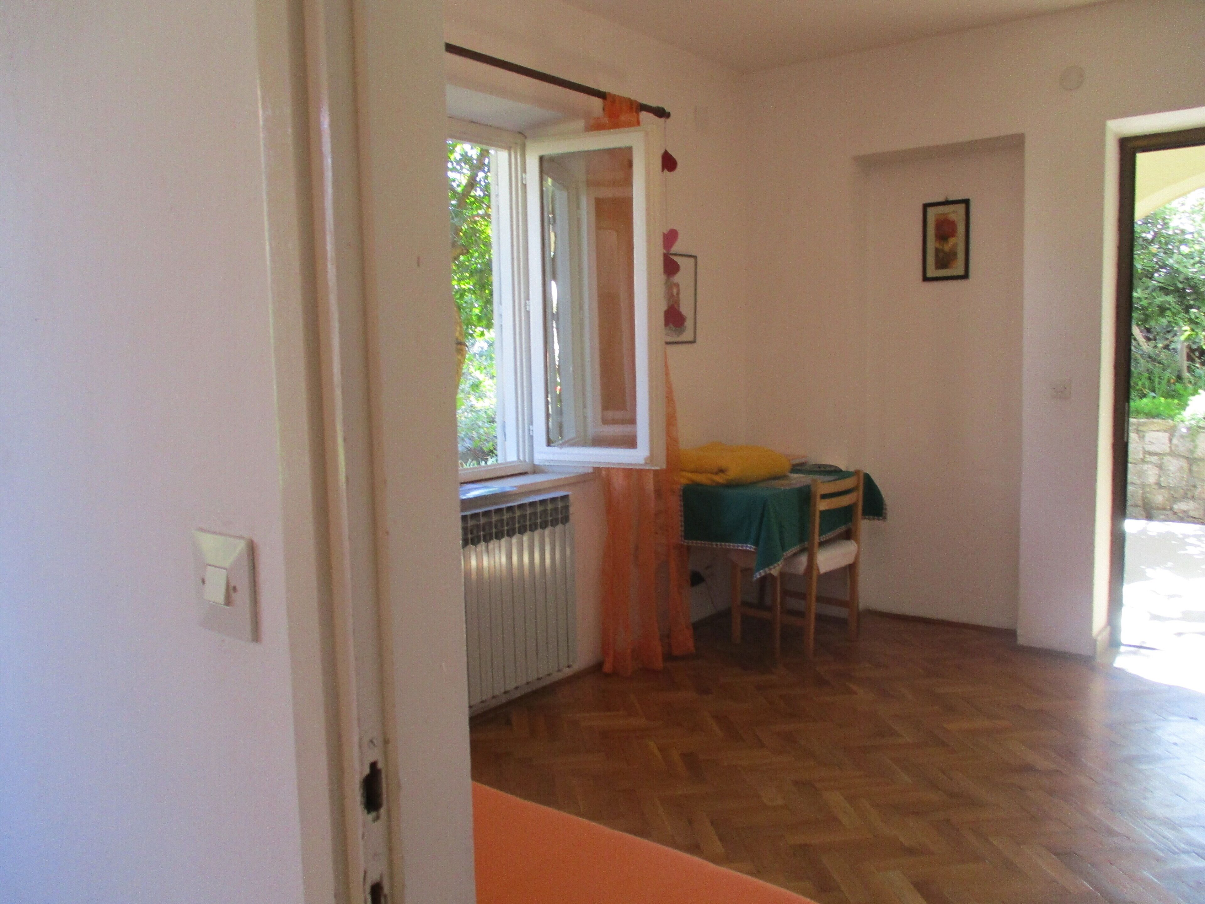 Une pièce avec un radiateur, une fenêtre avec des rideaux, une table recouverte d’une nappe verte et une chaise.