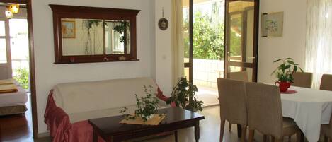 A living room with a sofa, a coffee table with a plant, and a dining area with chairs and a table.