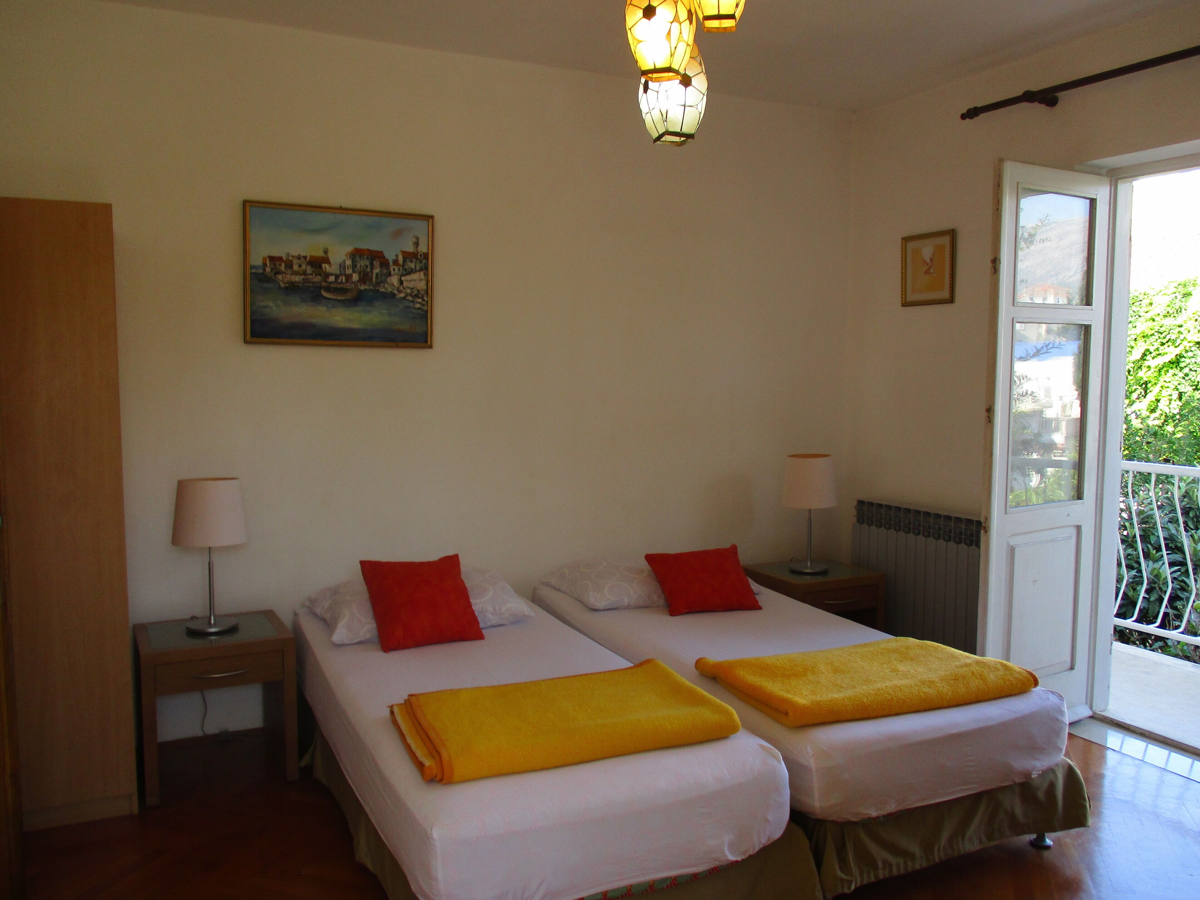 A room with two beds, each with a red and yellow pillow, and a painting on the wall.