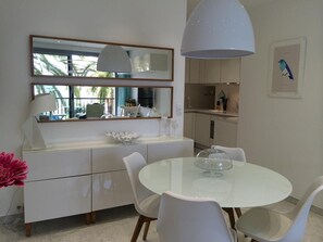 Cozinha moderna com armários brancos, uma mesa redonda de vidro e cadeiras brancas.