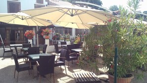 An outdoor seating area with tables and chairs under a large umbrella, surrounded by potted plants and flowers. - Gite Zuharpeta Randonneurs Pèlerins - Hostel (Saint-Jean-Pied-de-Port)