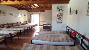 A room with multiple beds arranged in rows, wooden beams on the ceiling, and a door leading outside. - Gite Zuharpeta Randonneurs Pèlerins - Hostel (Saint-Jean-Pied-de-Port)