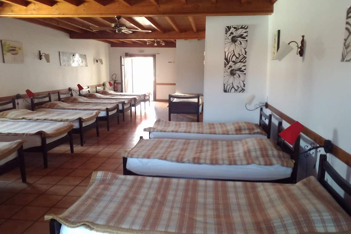 A room with multiple beds arranged in rows, wooden beams on the ceiling, and a door leading outside.