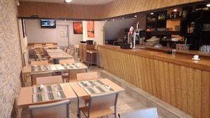 A restaurant with multiple tables and chairs, a bar area with a counter, and a television mounted on the wall. - Gite Zuharpeta Randonneurs Pèlerins - Hostel (Saint-Jean-Pied-de-Port)